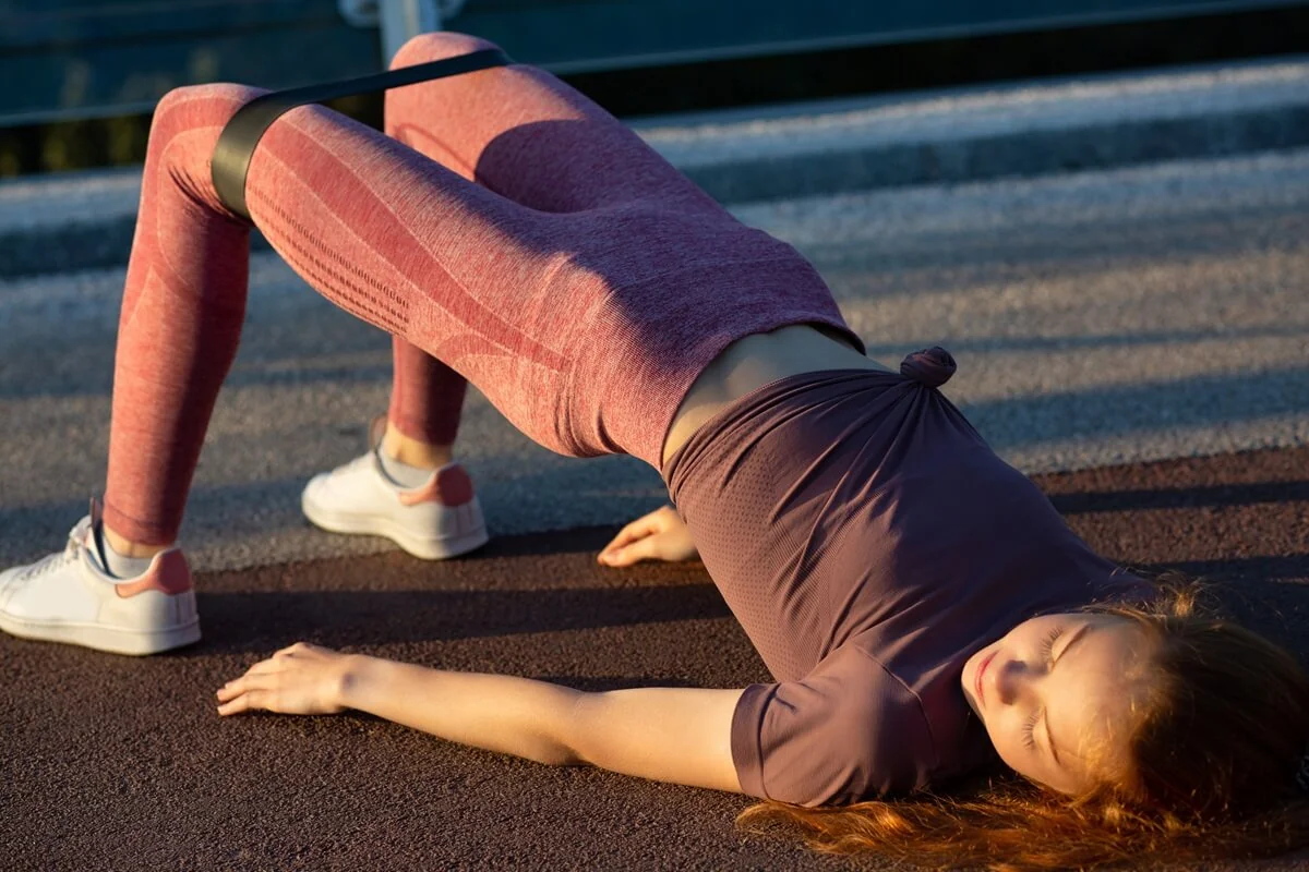 Žena cvičí glute bridge s odporovou gumou. Žena cvičí glute bridge s odporovou gumou.